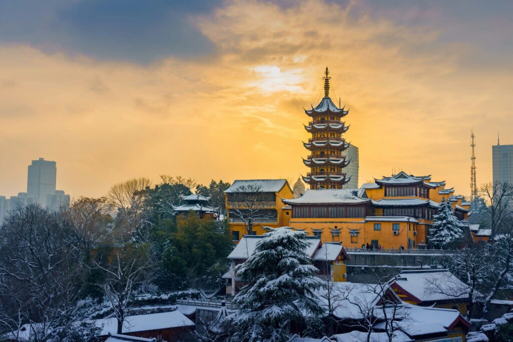 Pagoda tradicional china y templo rodeados de árboles nevados bajo un cielo al atardecer.
